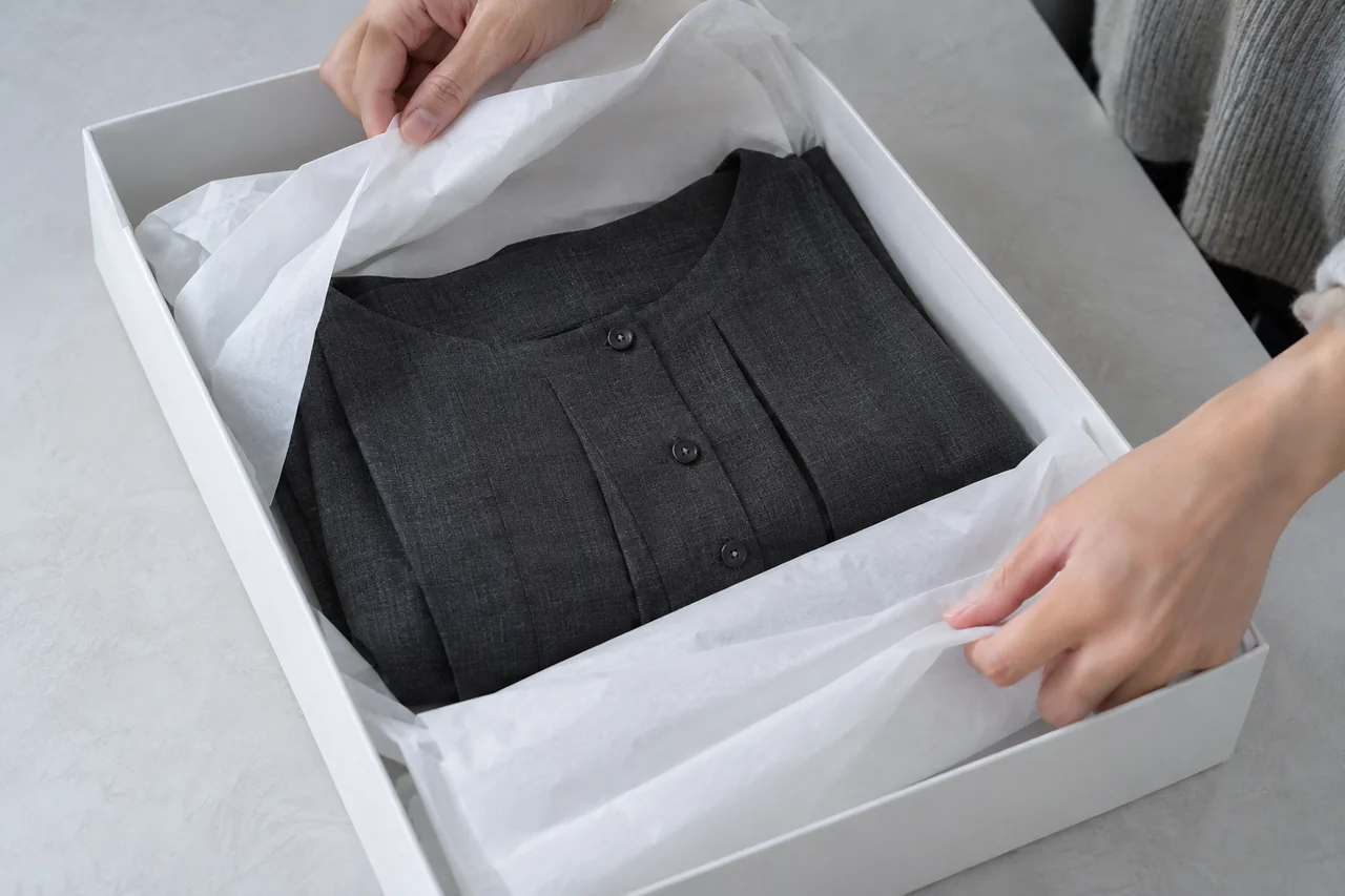 A finished charcoal garment being packed in a white tissue-lined box